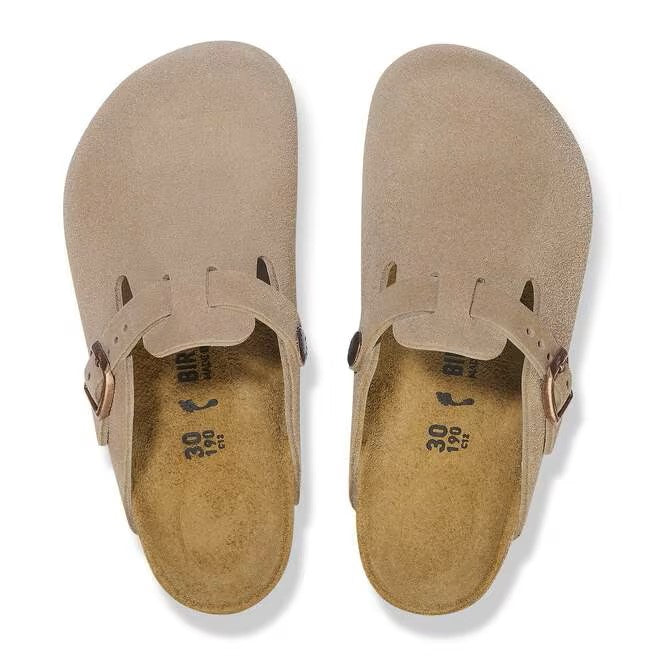 Two taupe-colored suede clogs seen from above, with adjustable buckle strap.