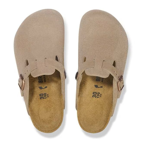 Two taupe-colored suede clogs seen from above, with adjustable buckle strap.