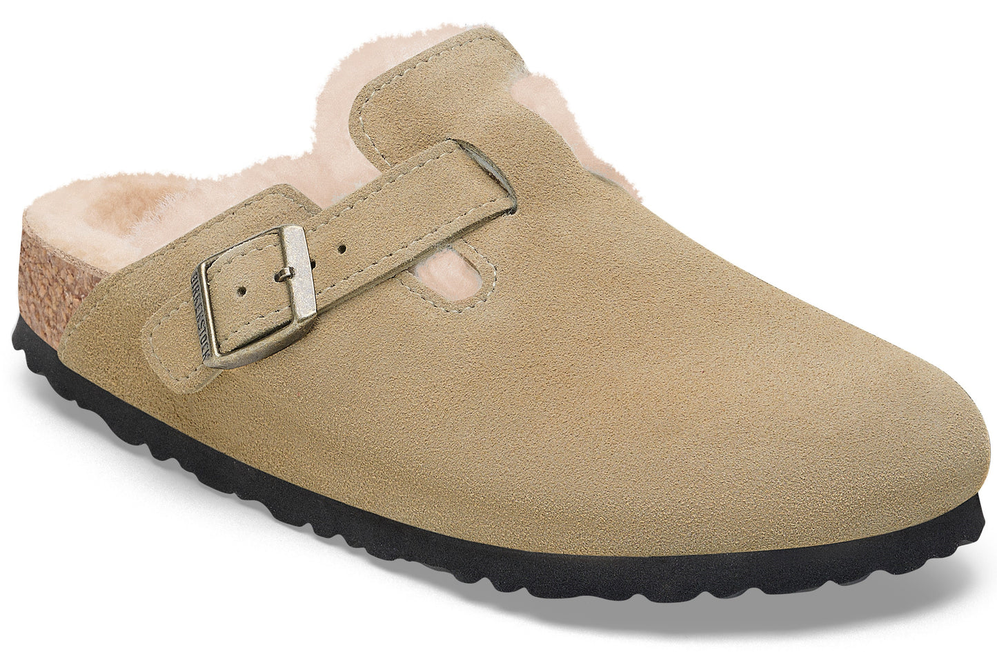 A tan suede slip-on shoe lined with cream-colored faux fur, featuring an adjustable side strap with a metallic buckle and a dark, textured rubber outsole.