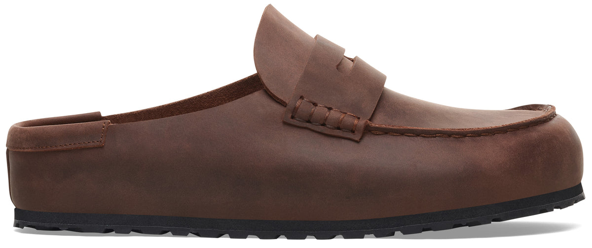 A brown leather backless loafer-style mule with a classic penny strap detail across the vamp and a black textured rubber sole.