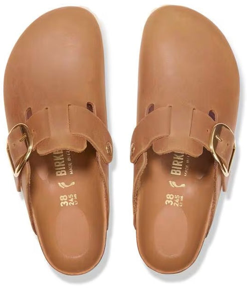 A pair of tan-colored leather backless slip-on clogs with a single metallic buckle strap across the top, showing the interior soles printed with size 38 and brand text.