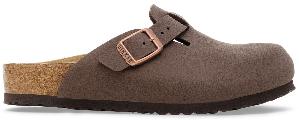 A brown slip-on clog shoe with a cork footbed and a single adjustable strap featuring a copper-toned metal buckle embossed with the word BIRKEN.
