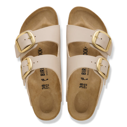Top-down view of two beige sandals with two straps and gold buckles.