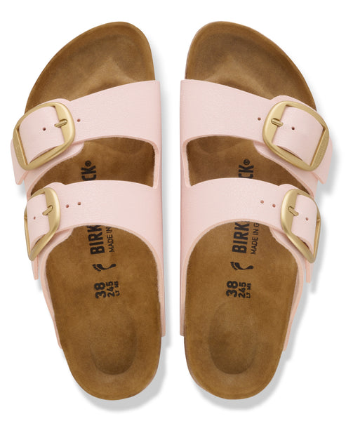 A pair of pink two-strap sandals with large gold buckles and brown footbeds.