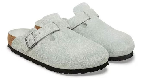 A pair of light-colored suede clogs with adjustable buckle straps and black soles.