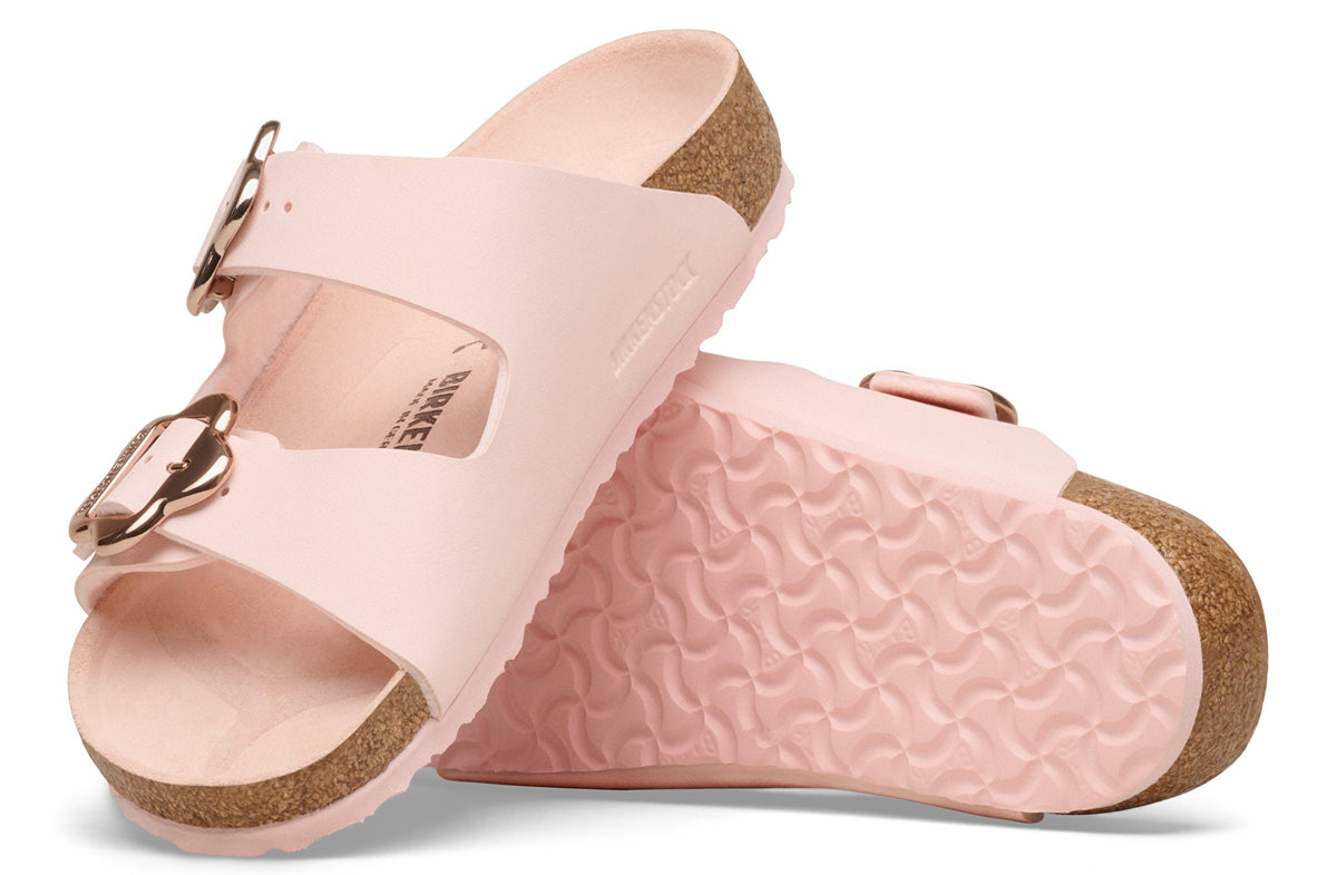 Two pink slide sandals with gold buckles; one is on its side, showing its sole.