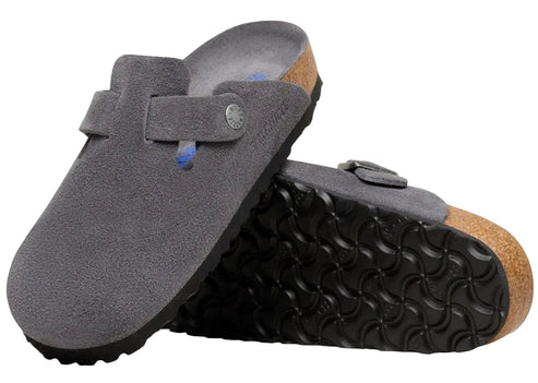 A pair of grey suede clogs featuring a contoured footbed with a cork midsole and a black textured rubber outsole, seen from an angle showing the upper of one shoe and the underside of the other.
