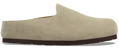 A slip-on mule shoe made of tan suede with a flat, dark brown rubber sole, shown in profile.