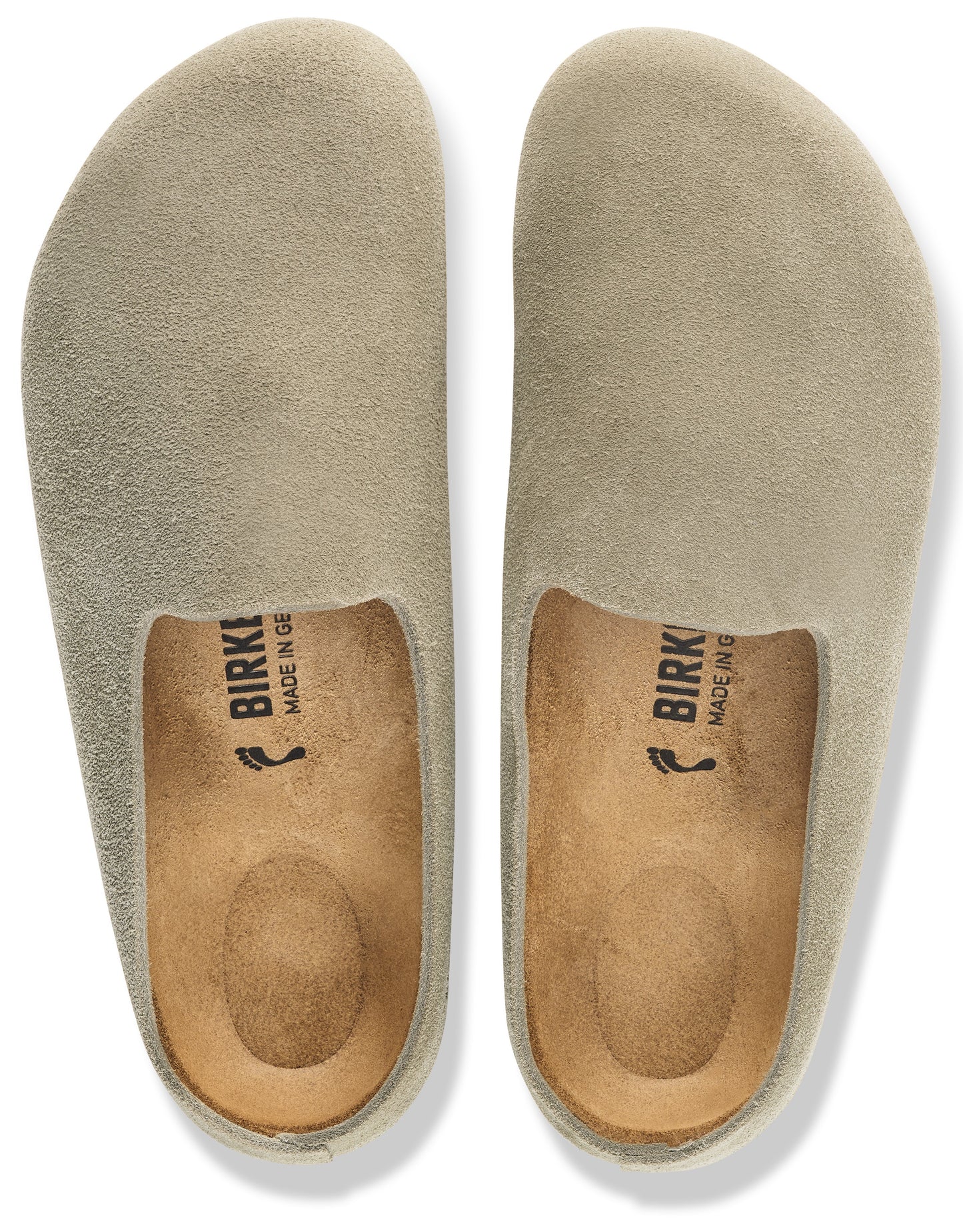 A pair of taupe suede slip-on shoes with a rounded toe, open heel, and cork-latex footbed with the text "BIRKENSTOCK MADE IN GERMANY" printed on the insole.