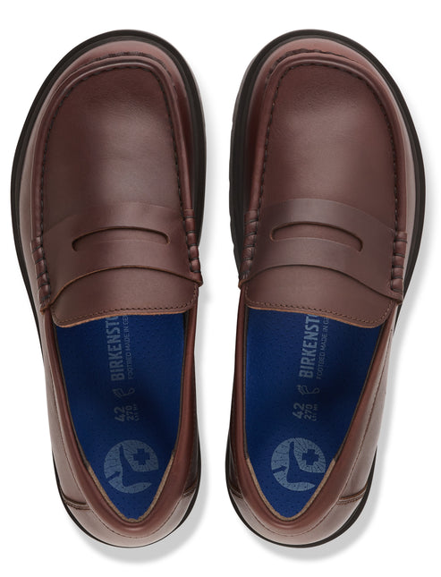 A pair of brown leather penny loafers shown from a top-down perspective, featuring blue insoles with a white foot icon and the text 'BIRKENSTOCK' printed on them.