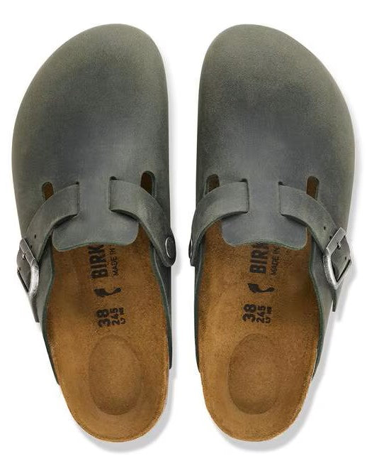 A pair of slate-grey suede leather clogs with an open back, featuring a side strap with a silver buckle, brown cork-latex footbeds with imprinted size 38, and Birkenstock brand text on a plain white background.