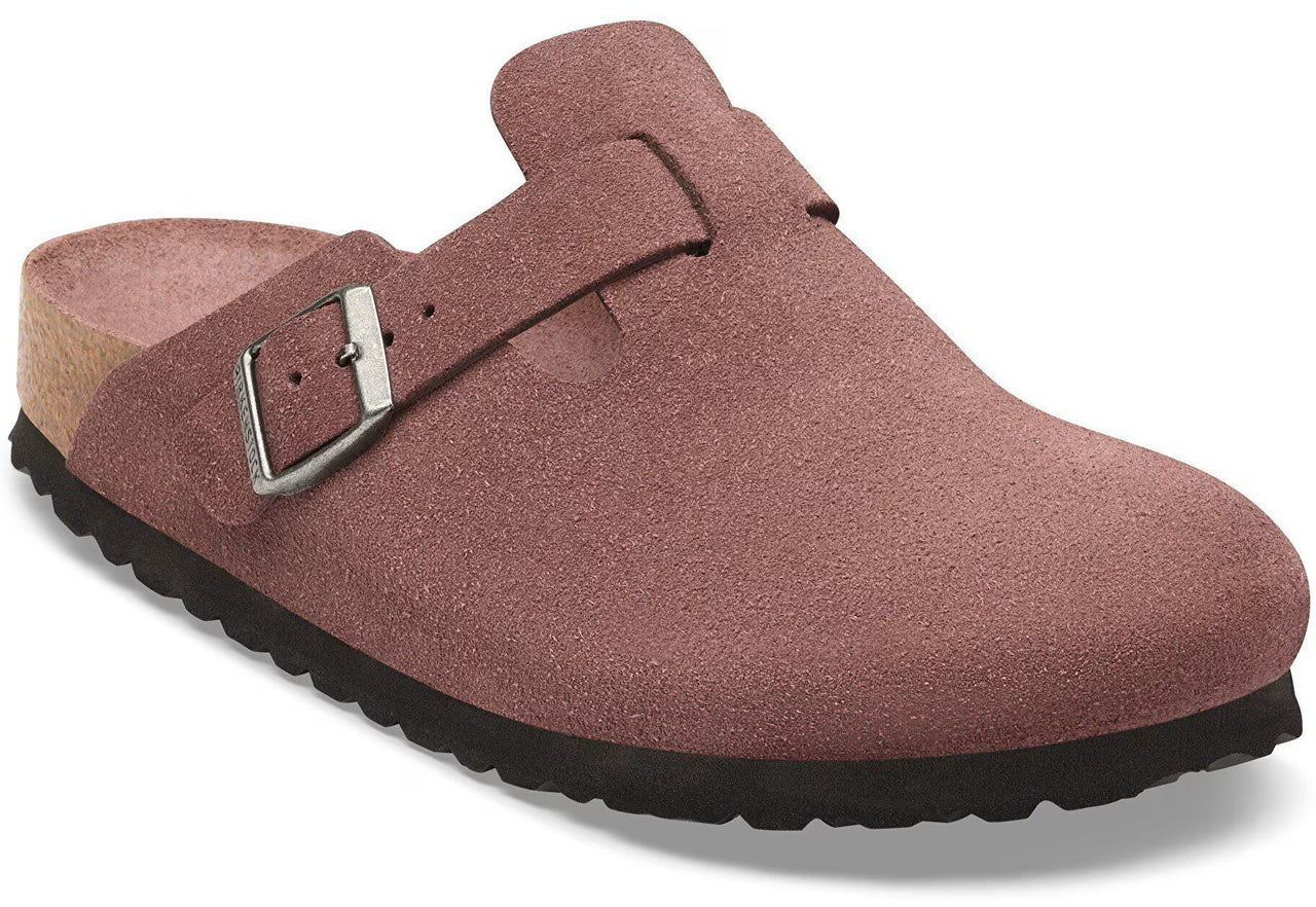 A dusty rose-colored suede clog featuring a side strap with a metallic buckle, a cork-textured footbed edge, and a black, ridged rubber sole.