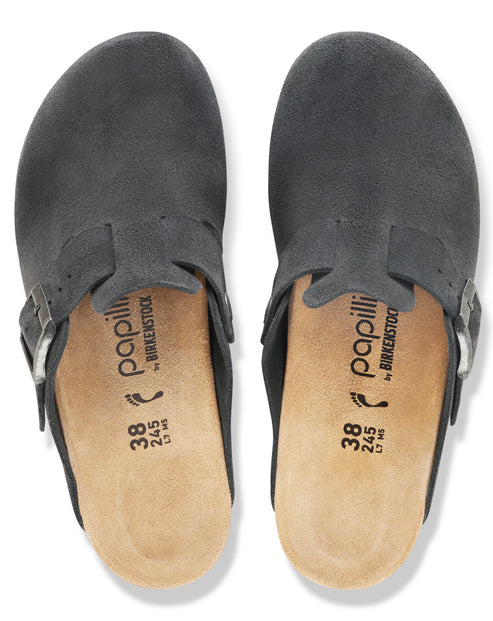 A pair of charcoal-colored suede closed-toe clogs shown from a top-down view, featuring adjustable side buckles and tan cork footbeds printed with sizing details and the brand logo.