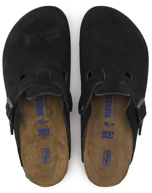 Overhead view of black suede clogs with adjustable straps and visible "BIRKEN" text inside.