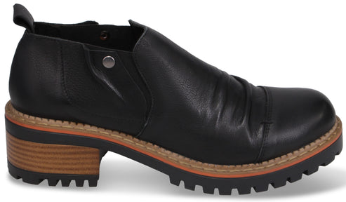 A black slip-on bootie with a ruched leather upper, a small silver rivet detail on the side, and a chunky, lug-style wooden-textured block heel with a tan and black stacked sole.