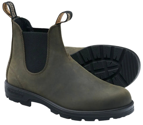 An olive green suede Chelsea boot with two pull tabs at the top, black elastic side panels, and a thick, black, lugged rubber sole. The brand name Blundstone is embossed on the side of the heel.