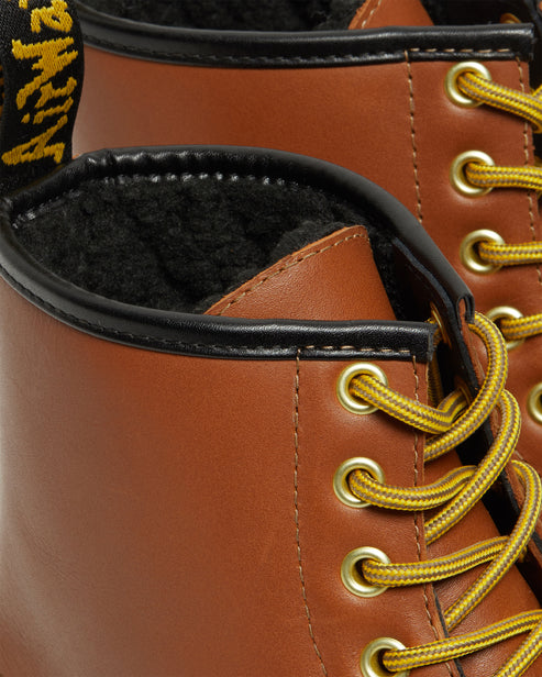 Close-up of a brown leather boot with yellow laces and gold eyelets, featuring a black-lined collar and black faux fur lining.