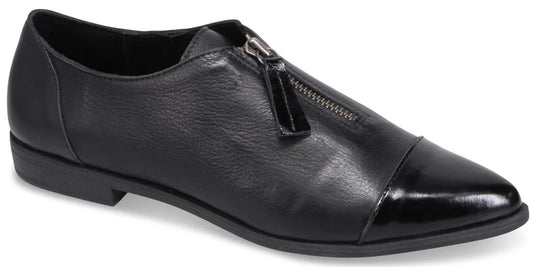 A black leather flat shoe with a pointed toe, a patent leather cap toe, and a center zipper closure with a rectangular pull tab.