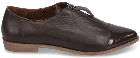 A brown leather, flat, zipper-front shoe with a dark, glossy patent leather toe cap and a low, tan-colored sole.