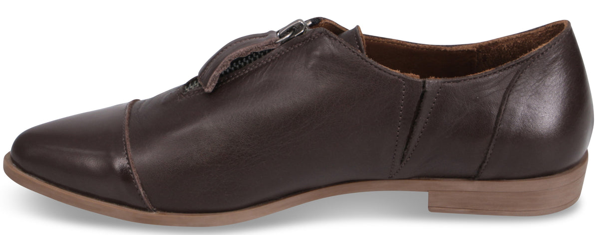 A dark brown leather cap-toe flat shoe with a center front zipper closure and a low, light tan rubber heel, viewed from the side.