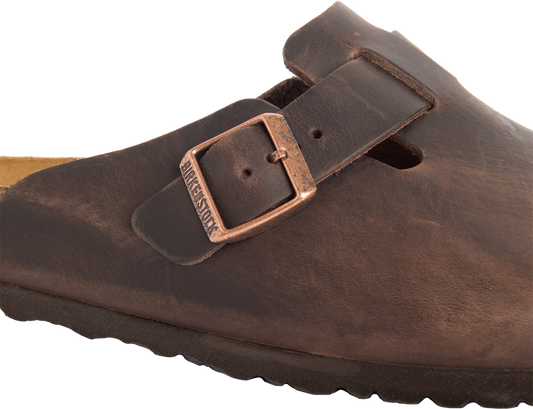 Close-up of a brown leather sandal with a copper-colored metal buckle labeled 