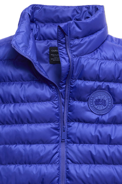 Close-up of a bright blue, quilted vest with a high collar and a circular patch on the right breast.