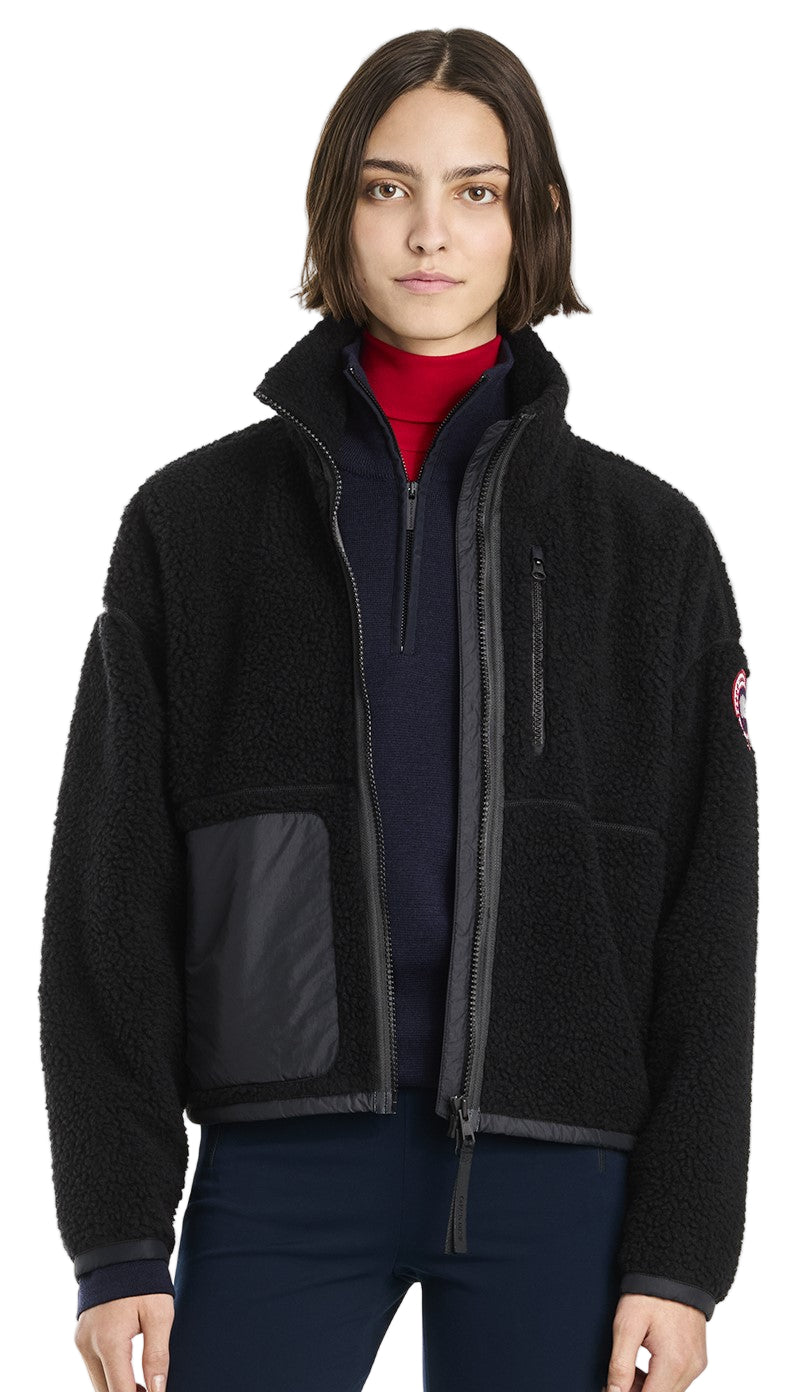A person wears a black, fuzzy, fleece zip up jacket with a utility pocket on the left side.