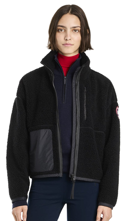 A person wears a black, fuzzy, fleece zip up jacket with a utility pocket on the left side.