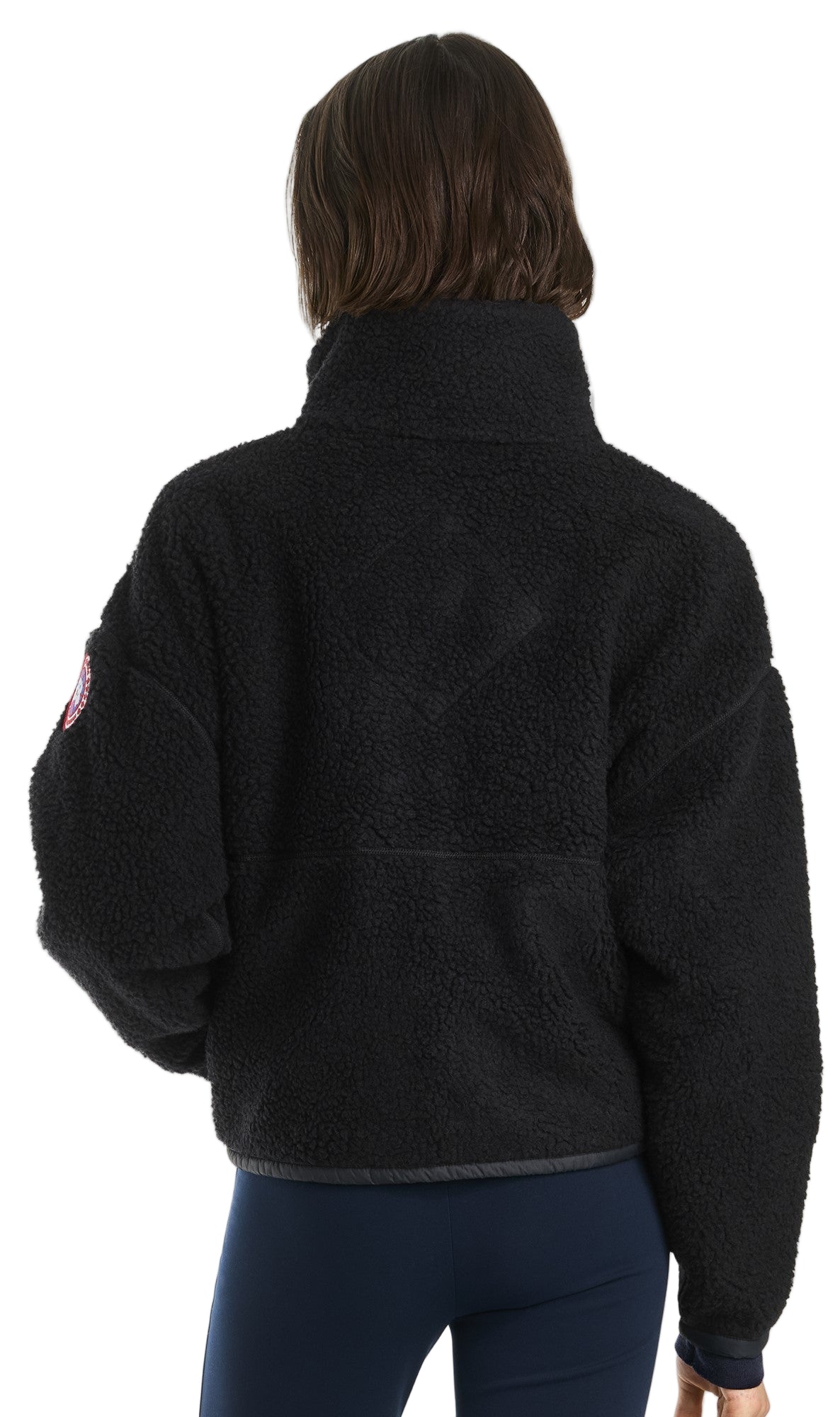 Back view of a dark-colored, fleece, pullover jacket with a tall collar and an emblem on the left sleeve.