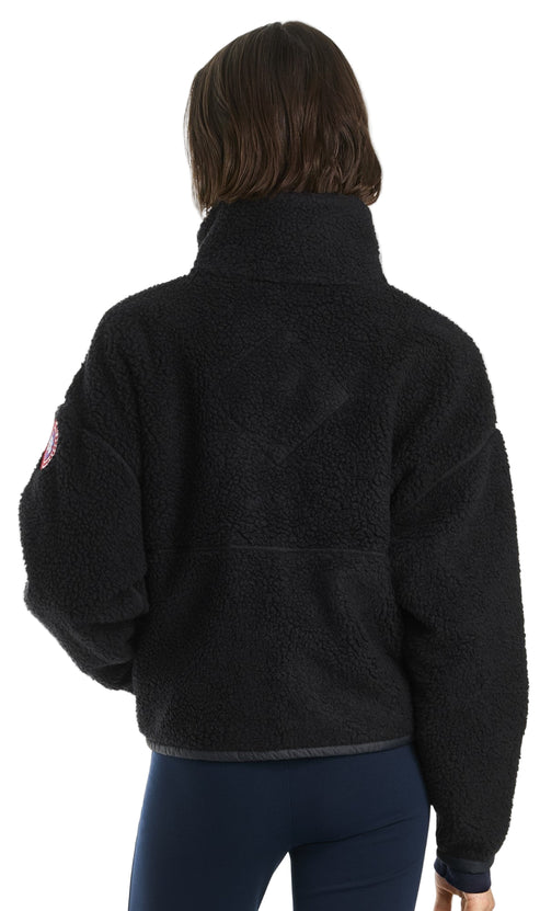 Back view of a dark-colored, fleece, pullover jacket with a tall collar and an emblem on the left sleeve.