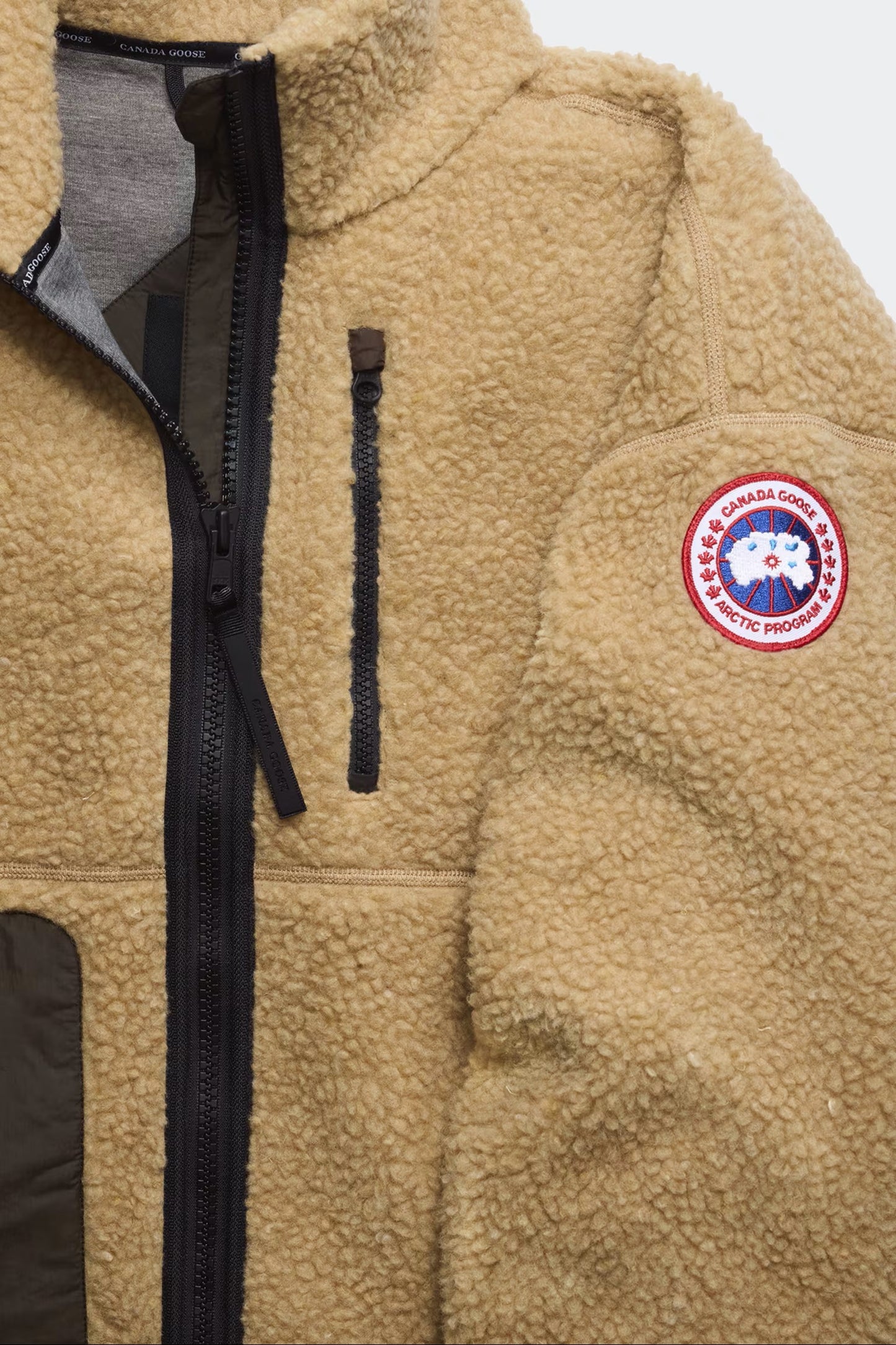 Tan fleece jacket with full zipper, zippered chest pocket, and circular Canada Goose patch on sleeve.