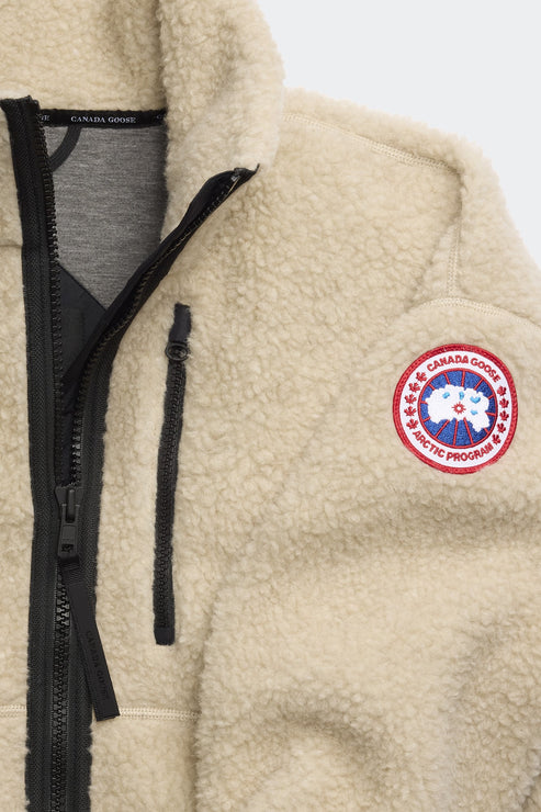 Close-up of a cream sherpa jacket with black zipper, chest pocket, and a circular patch with a maple leaf.