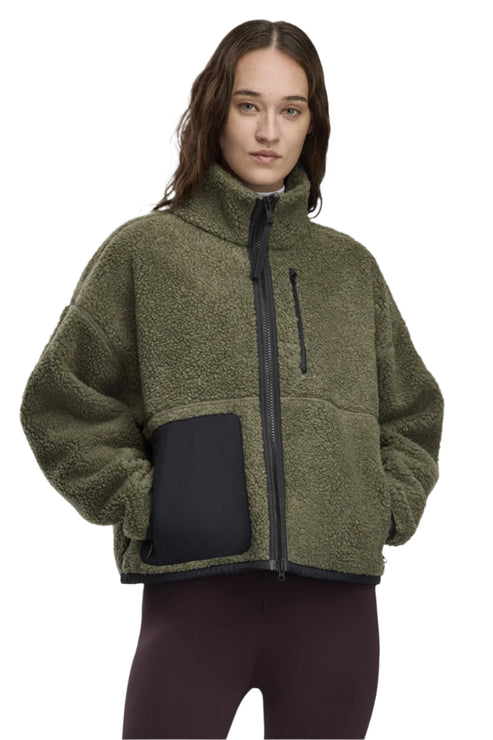 Woman wearing an olive green, full-zip, faux-shearling jacket with a black chest pocket.
