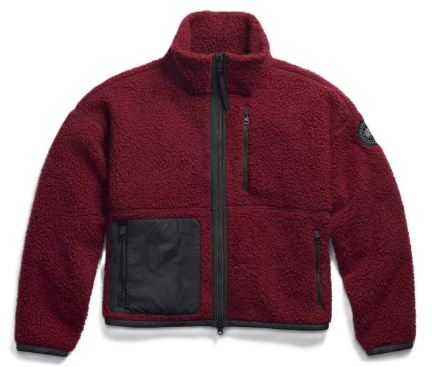 A deep burgundy fleece zip-up jacket with a high collar, featuring a black zippered chest pocket, two lower zippered pockets, black trim, and a small circular logo patch on the left sleeve.