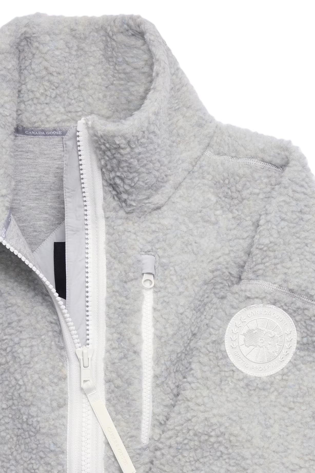 Close-up of gray sherpa fleece jacket with a white zipper and a round emblem.