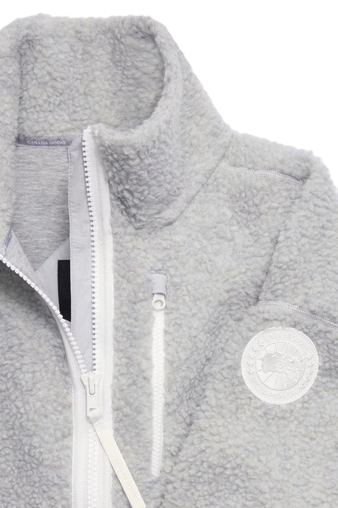 Close-up of gray sherpa fleece jacket with a white zipper and a round emblem.