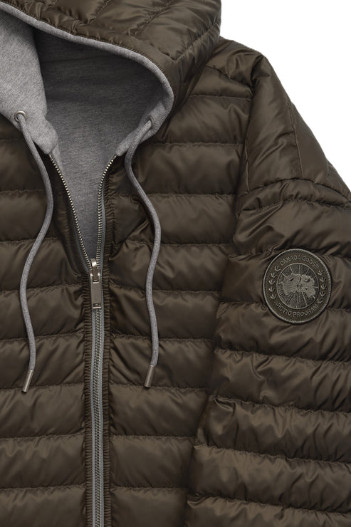 Close-up of a puffy, brown, hooded jacket with a gray hood and silver zipper. The sleeve has a round, dark-colored emblem.