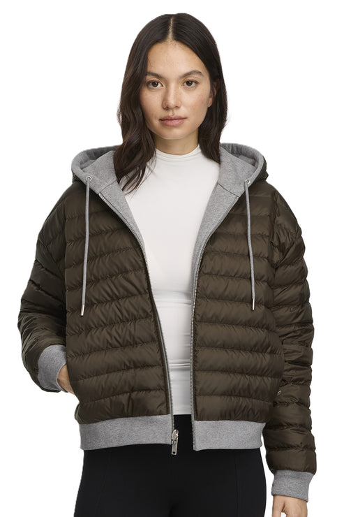 A woman wearing a short, olive-green puffer jacket with a light gray hood and trim.