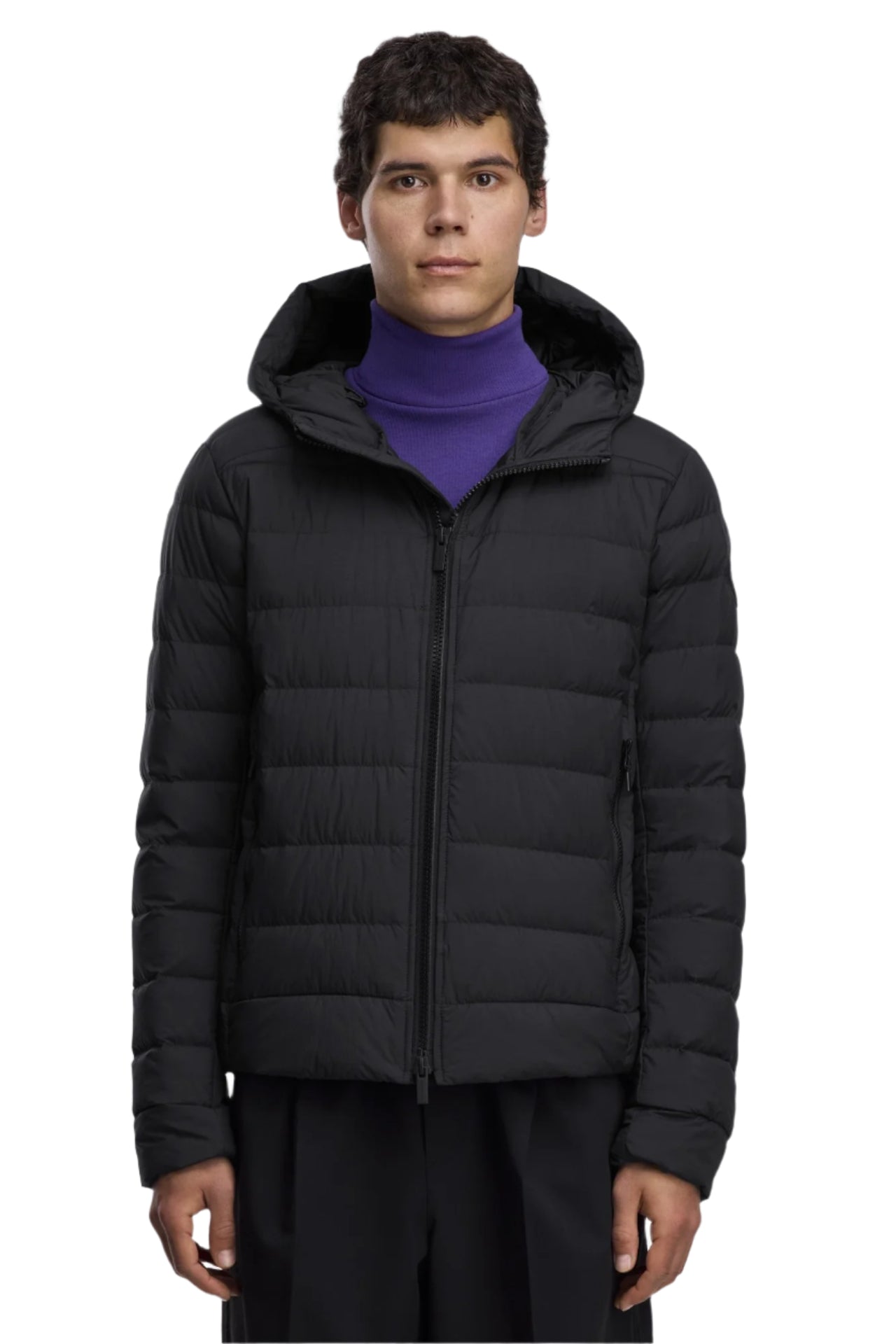 A man wearing a black hooded puffer jacket, zipped up, with a purple turtleneck sweater underneath.