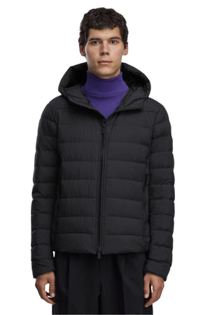 A man wearing a black hooded puffer jacket, zipped up, with a purple turtleneck sweater underneath.