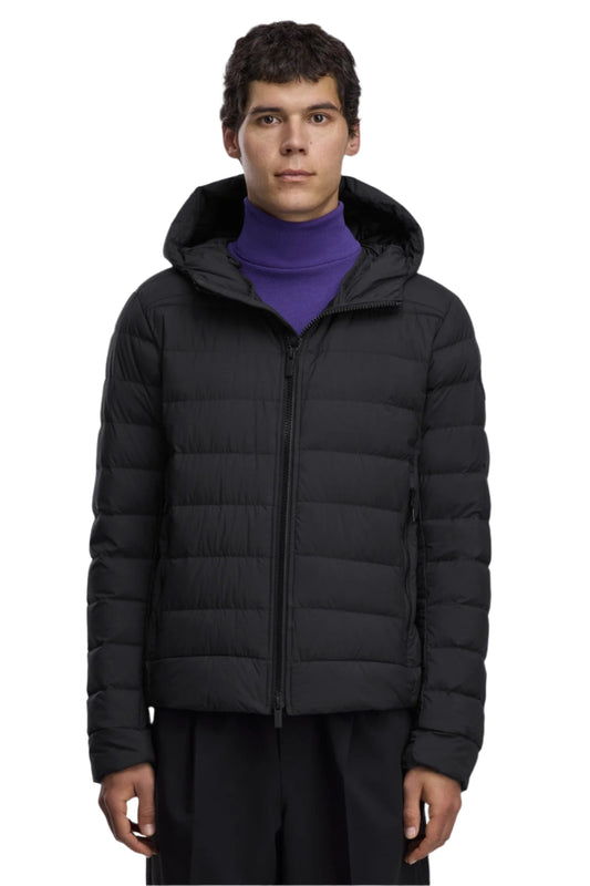 A man wearing a black hooded puffer jacket, zipped up, with a purple turtleneck sweater underneath.