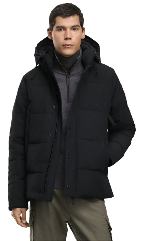 A man wearing a black puffer jacket with a hood and gray pants.