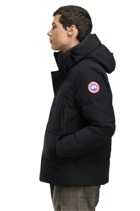 Man wearing a black puffer jacket with a hood and circular logo on the arm.