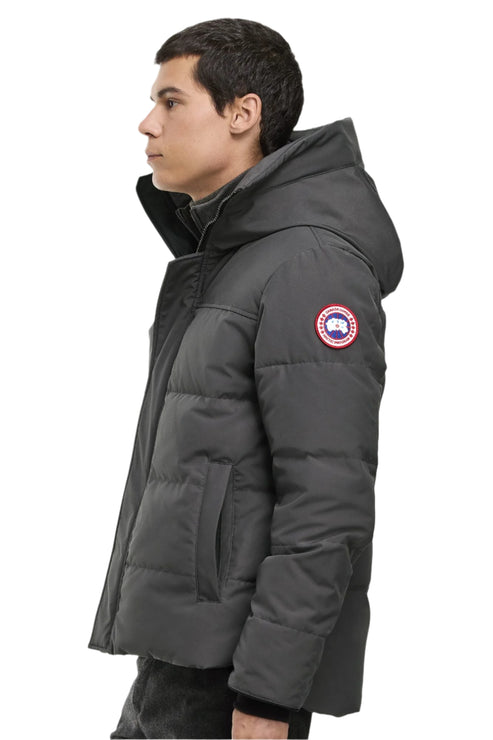 A man in a short, grey, puffy coat with a hood and a circular patch on the upper left arm.