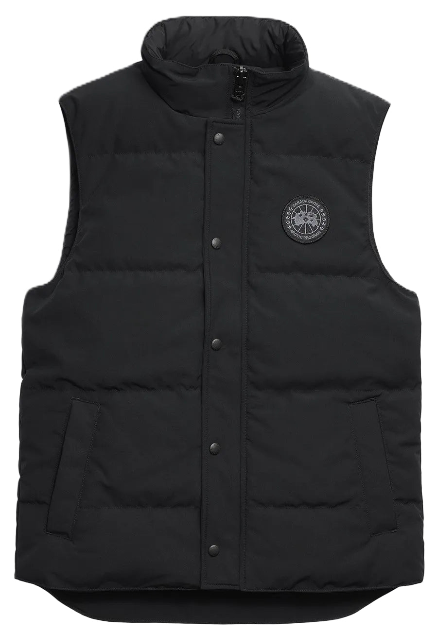 A black quilted puffer vest with a high collar, a central snap-button placket, two side pockets, and a round black and grey circular patch on the left chest.