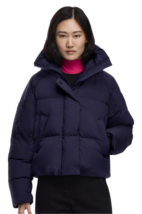 A woman wears a short, navy puffer jacket with a wide collar and a pink turtleneck.