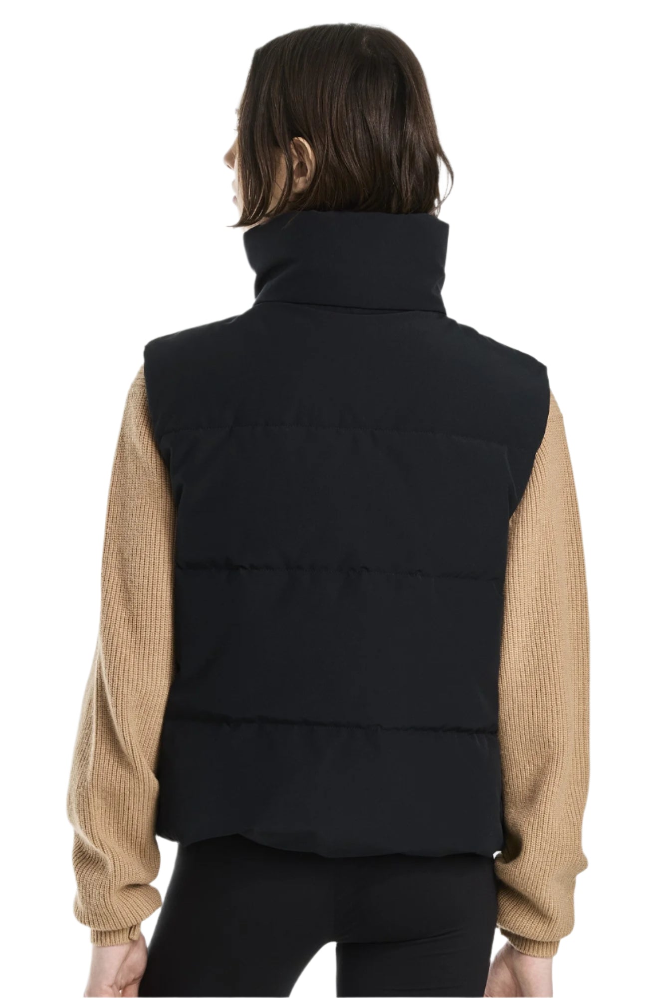 A person with short hair is facing away from the camera wearing a black puffy vest with a tall collar over a tan-colored sweater.