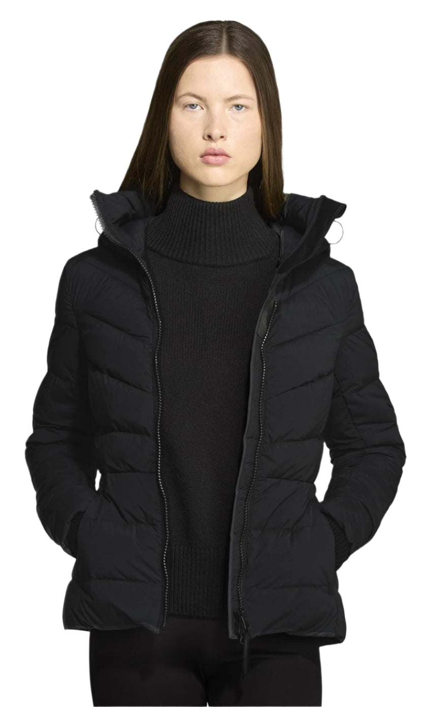 A woman is wearing a short, black, puffer jacket with a hood and her hands in the pockets.