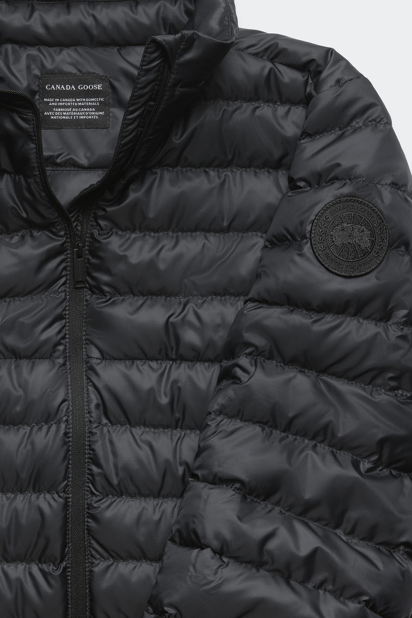 Close-up of a black, quilted down jacket with a round logo patch on the sleeve and a visible label.