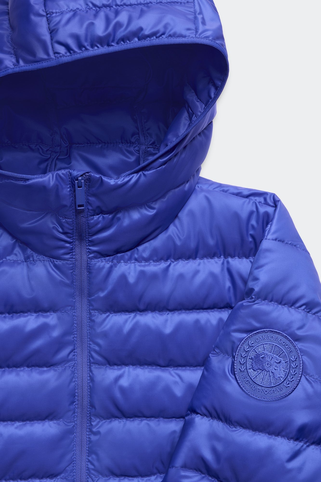 Close-up of a blue puffer jacket featuring a circular logo on the sleeve and a hood.